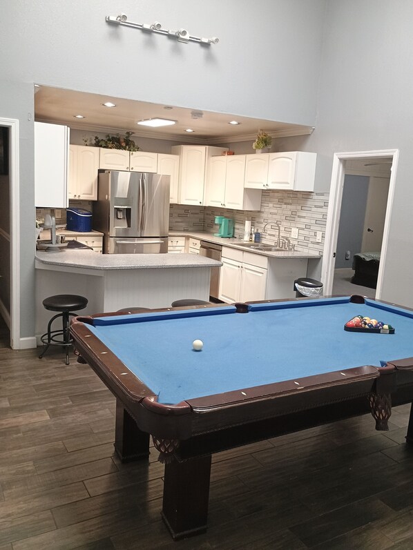 Une table de billard dans une pièce qui comprend un coin cuisine, avec un réfrigérateur et des placards.
