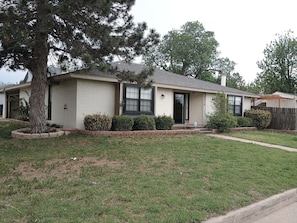 A single-story house with a brick exterior, a front porch, and a large tree in the front yard.