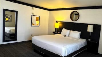 A hotel room with a large bed, a bedside table with a lamp, a mirror, and a framed picture on the wall.