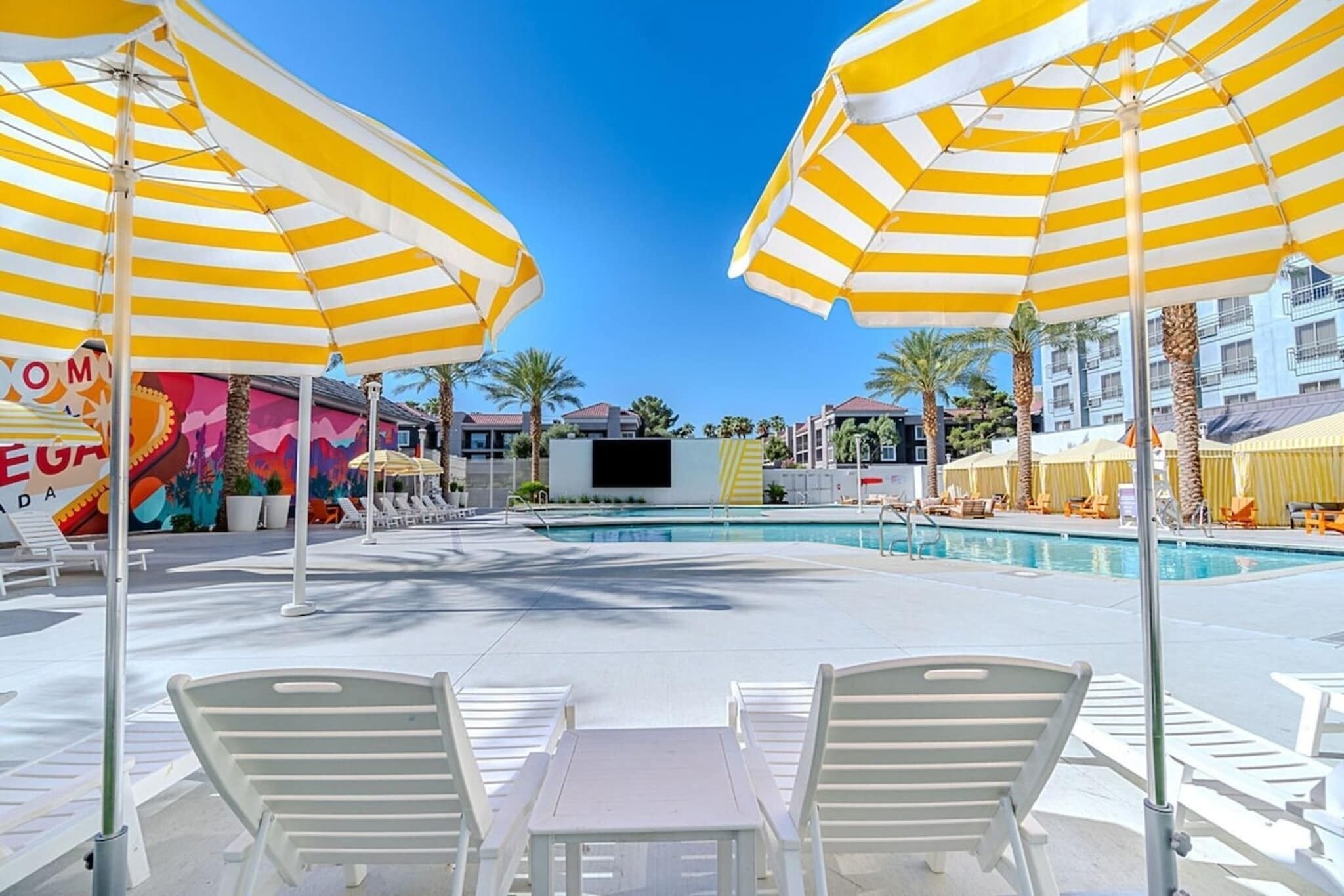 A poolside area with striped umbrellas, lounge chairs, and a mural.