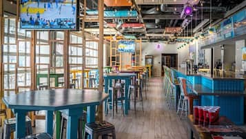 A bar area with tables and stools, a television screen, and a bar counter.