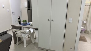 A compact living space with a kitchenette, a dining area with a table and chairs, and a wardrobe. - Ravello Residential AP03 Foz do Iguaçu (Foz do Iguaçu)