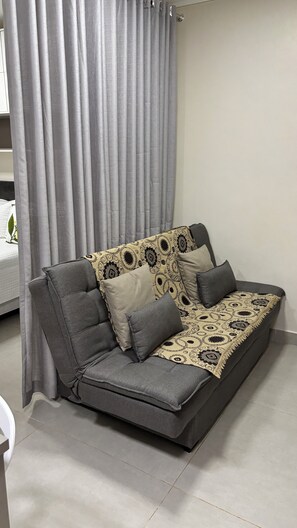 A grey sofa with patterned cushions, a grey curtain, and a white wall. - Ravello Residential AP03 Foz do Iguaçu (Foz do Iguaçu)