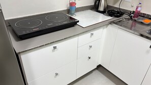 A kitchen with a black induction cooktop, white cabinets, a stainless steel kettle, and a water bottle on the counter. - Ravello Residential AP03 Foz do Iguaçu (Foz do Iguaçu)