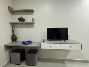 A modern room with a flat-screen TV, a potted plant, a blue cushion, and two storage bins. - Ravello Residencial – Comfort and tranquility in Foz do Iguaçu (Foz do Iguaçu)