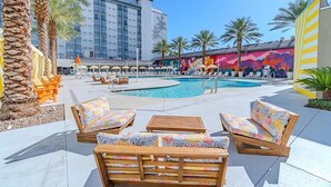 Un espace piscine avec des chaises longues, une fresque murale et, au fond, le bâtiment de l’hôtel.