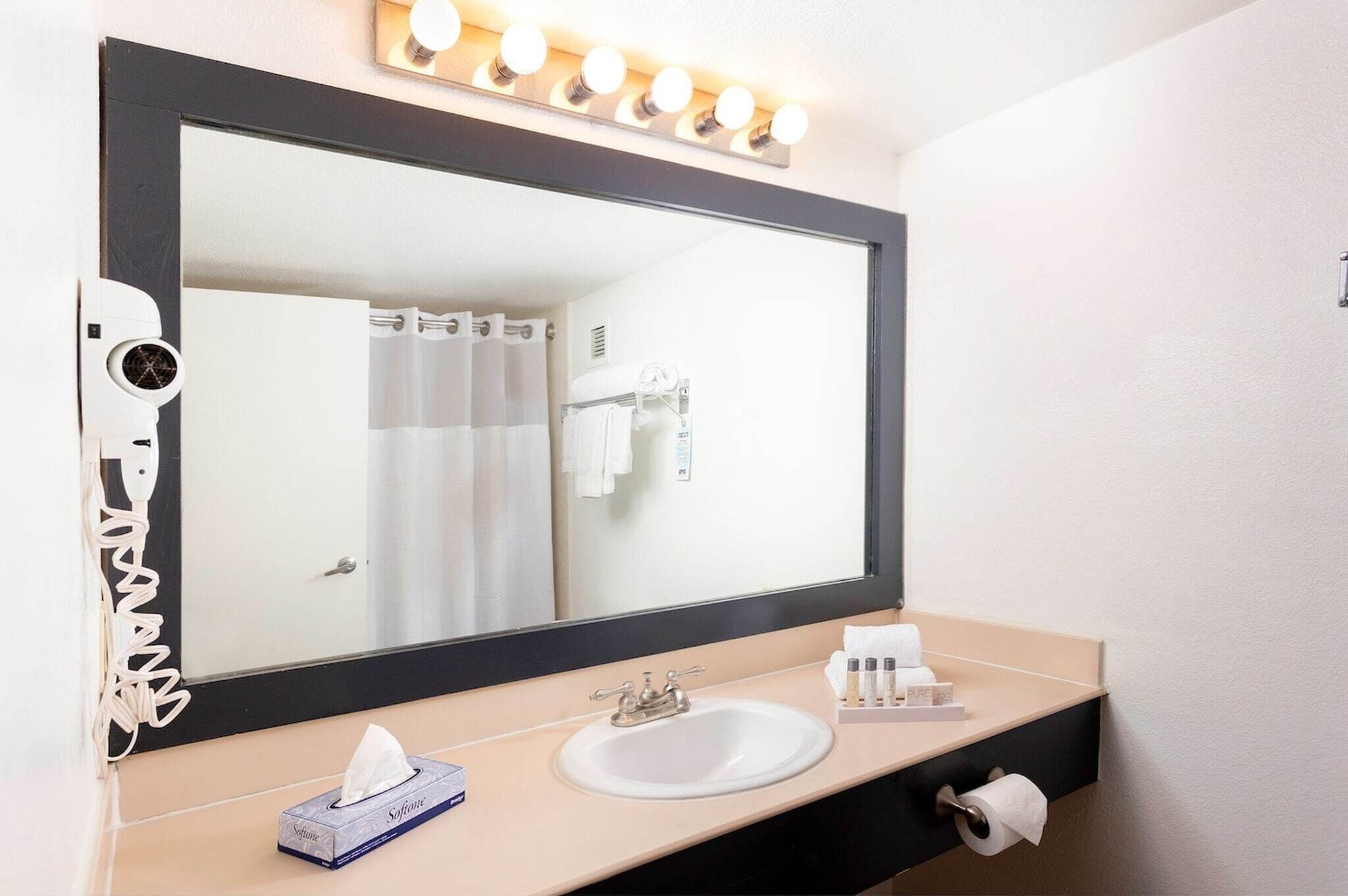 A bathroom with a large mirror, a sink, a hairdryer, and a towel rack.