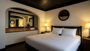 Habitación de hotel con una cama grande, dos lámparas de noche, un espejo redondo y un cabecero de madera.
