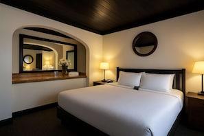 A hotel room with a large bed, two bedside lamps, a round mirror, and a wooden headboard.