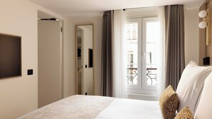 A hotel room with a bed, a TV, a balcony with a railing, and a door leading to another room. - Modern Apartment a/c 1BR/2P - Saint-Germain (Paris)