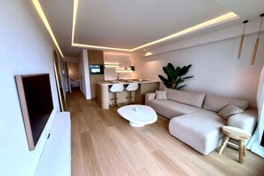 Ein modernes Wohnzimmer mit einer Couch, einem Couchtisch, einem Fernseher und einer Küchenzeile mit Essplatz.