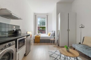A compact living space with a kitchenette, a bed with a view, a sofa, and a small table. - Standard Studio (London)