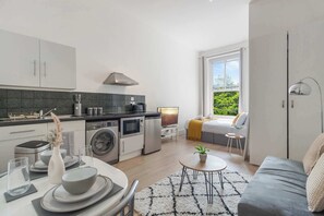 A modern kitchen with a dining area, a sofa, and a view of greenery outside. - Standard Studio (London)