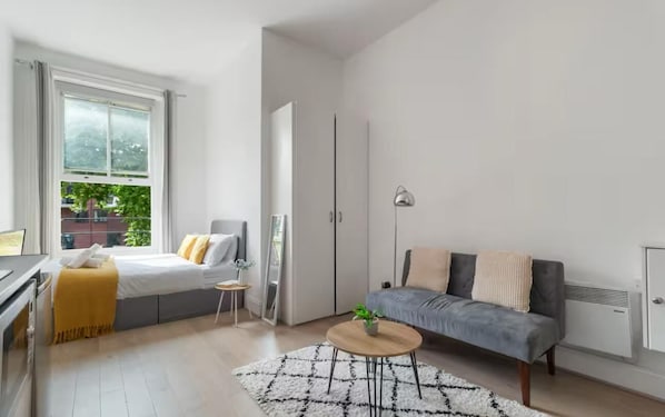 A modern, minimalist bedroom with a bed, bedside table, and a view of greenery outside. - Standard Studio (London)
