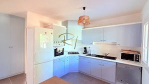 Une cuisine compacte avec des meubles blancs, un four encastré, un four à micro-ondes et un luminaire suspendu.