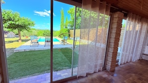 Une pièce dotée d’une grande porte-fenêtre coulissante donnant sur un jardin avec une piscine, des chaises et une pelouse.