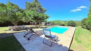 Une piscine avec des chaises longues, une table et un espace herbeux agrémenté d’arbres.
