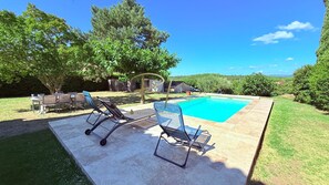 A swimming pool with lounge chairs, a table, and a grassy area with trees.