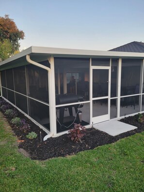 Un patio cubierto con una parrilla, una puerta corrediza de vidrio y un pequeño escalón que lleva a la puerta.