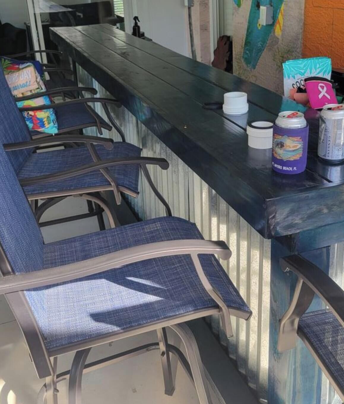 Uma área de bar com cadeiras estofadas em azul, um balcão com uma lata de bebida e uma chávena rosa, e uma parede com um mapa.
