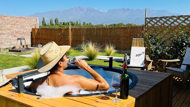 Une personne se détend dans un bain à remous en bois, avec une vue sur les montagnes en arrière-plan.