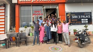 A group of people in front of a hotel named 'Hotel Shri Ji Palace' with a sign indicating rooms available. - Hotel Shri Ji Palace (Rajnagar)