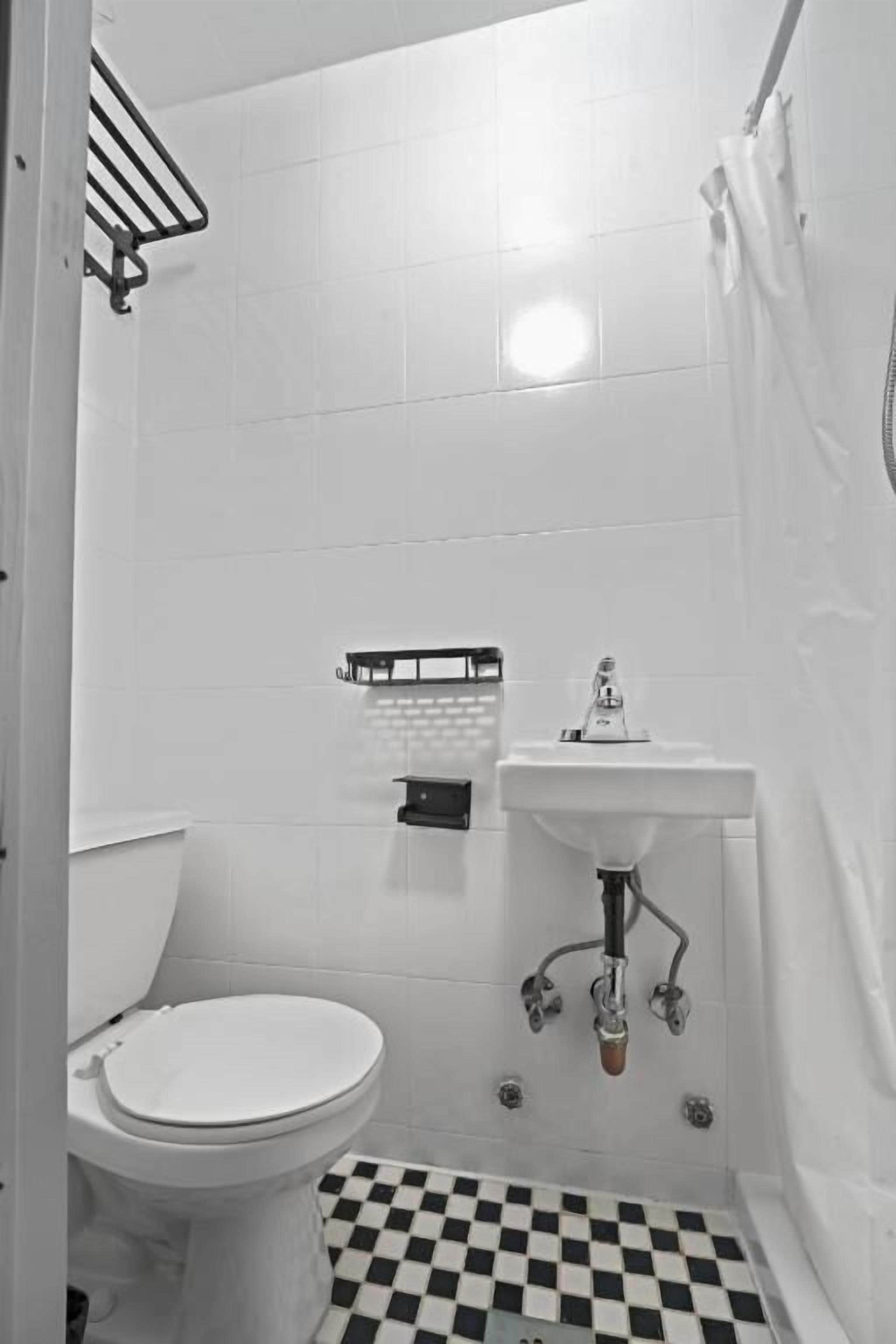 Une petite salle de bain blanche, équipée de toilettes, d’un lavabo et d’un espace douche.