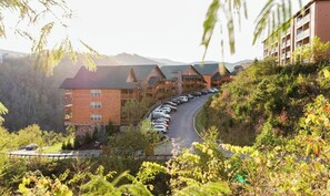 Et hotel med flere bygninger, parkeringsplads og et bjerglandskab i baggrunden.