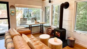 A cozy cabin interior with a sofa, round tables, a fireplace, and large windows.