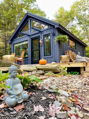 Une cabane moderne dotée d’une grande fenêtre, d’une terrasse et d’une statue de Bouddha dans le jardin.