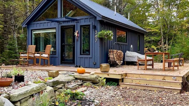 A blue cabin with a deck, wooden chairs, and a table.
