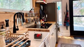 A compact kitchen with wooden walls, a window, and a door leading outside.