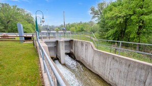 Ein Kanal aus Beton mit Metallgeländer, umgeben von Grünpflanzen und Bäumen.