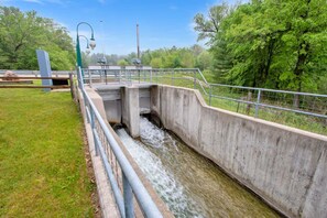 A concrete water channel with a metal railing, surrounded by greenery and trees. - 2-bedroom mill in adorable Wautoma with AC and charm (Wautoma)
