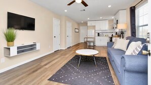 A modern living room with a ceiling fan, a flat-screen TV, a blue sofa, and a dining area with a table and chairs. - Cozy 1-bedroom apartment in enjoyable Houston with AC (Houston)
