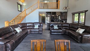 A spacious living area with leather sofas, wooden chairs, a wooden staircase, and a kitchen in the background. - Mountain Home in Gallatin Canyon with Home Theater and 3 Spacious BR/BA (Gallatin Gateway)