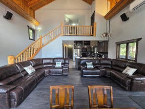 A spacious living area with leather sofas, wooden chairs, a wooden staircase, and a kitchen in the background. - Mountain Home in Gallatin Canyon with Home Theater and 3 Spacious BR/BA (Gallatin Gateway)