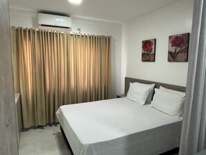 A hotel room with a bed, curtains, an air conditioning unit, and two wall-mounted flower paintings. - Ravello Residential AP04 Foz do Iguaçu (Foz do Iguaçu)