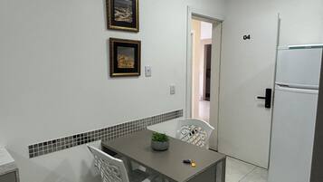Uma pequena cozinha compacta com geladeira, uma mesa de jantar com cadeiras e duas fotos emolduradas na parede.