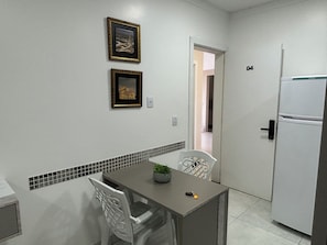 A small kitchenette with a refrigerator, a dining table with chairs, and two framed pictures on the wall. - Ravello Residential AP04 Foz do Iguaçu (Foz do Iguaçu)
