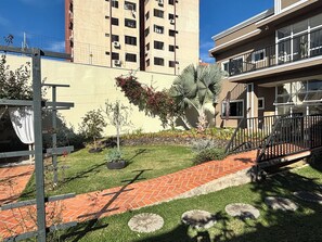 A courtyard with a brick pathway, a palm tree, and a small garden area. - Ravello Residential AP04 Foz do Iguaçu (Foz do Iguaçu)