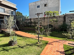 A courtyard with a brick pathway, a small tree, and a building with a stone wall. - Ravello Residential AP04 Foz do Iguaçu (Foz do Iguaçu)