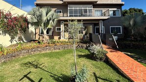 A two-story residential building with a balcony, a stone wall, and a well-maintained garden with various plants and a brick pathway. - Ravello Residential AP04 Foz do Iguaçu (Foz do Iguaçu)