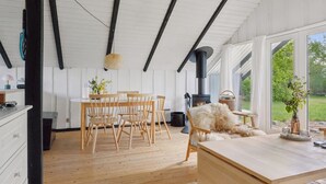 Ein gemütliches Zimmer mit Holztisch, Stühlen, einer Couch und einem großen Fenster mit Blick ins Freie.