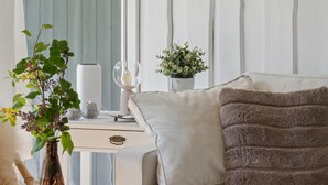 Ein Zimmer mit einem Bett, einem Nachttisch mit Vase und Kerzen, einem Fenster mit Vorhängen und einer Pflanze auf der Fensterbank.