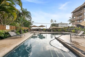 Ein Swimmingpool mit Liegestühlen und Sonnenschirmen, umgeben von Palmen und einem Holzzaun.