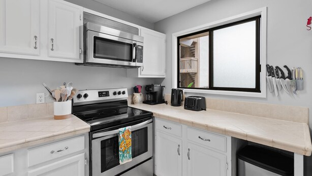 A kitchen with white cabinets, a microwave, stove, oven, and a window with a view of a balcony. - Royal Kahili B204 AC Across From Lymans/banyans (Kailua-Kona)