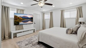 Una camera da letto con un letto, una ventola a soffitto, una TV e una finestra con tende.