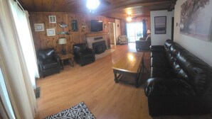 Quarto com painéis de madeira, lareira, sofás de couro e uma televisão.