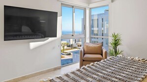Una habitación moderna con un televisor montado en la pared, un sofá de cuero, un tapete estampado y un balcón con vista a la piscina.